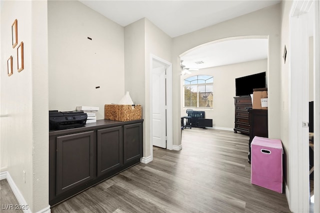 hallway with baseboards, arched walkways, and dark wood-style flooring