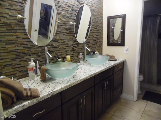 full bath featuring toilet, tasteful backsplash, double vanity, and a sink