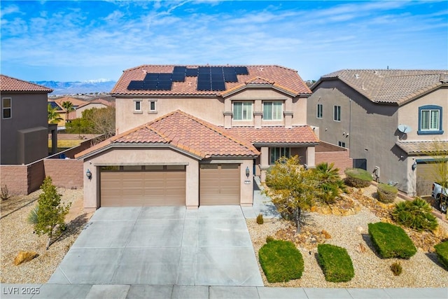 mediterranean / spanish-style house with a garage, a tile roof, concrete driveway, roof mounted solar panels, and stucco siding