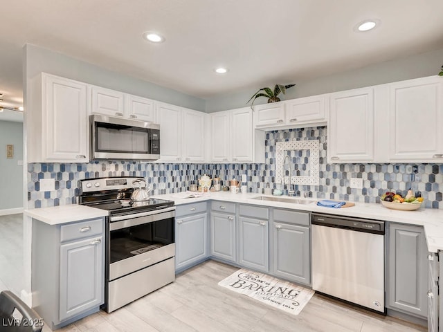 kitchen with a sink, gray cabinets, stainless steel appliances, light countertops, and backsplash