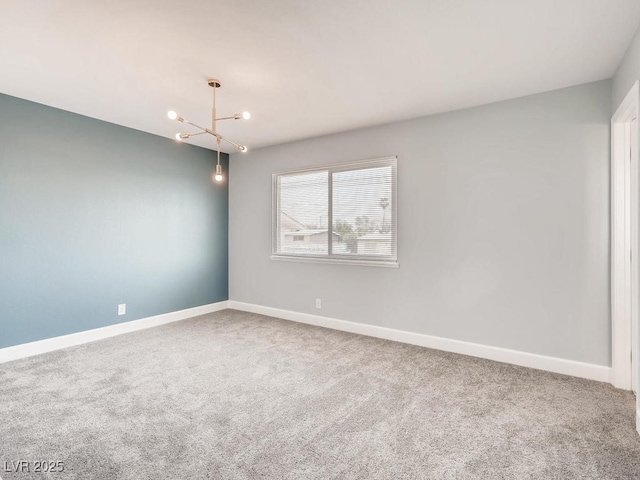 carpeted empty room featuring a notable chandelier and baseboards