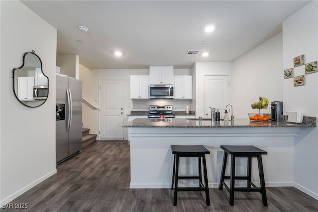 kitchen featuring stainless steel appliances, visible vents, white cabinetry, dark stone countertops, and a peninsula