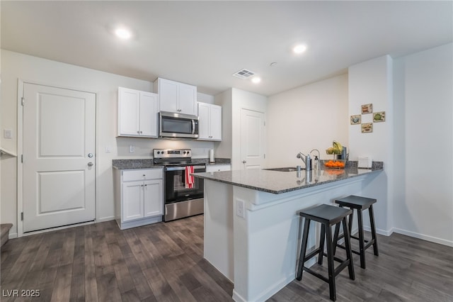 kitchen featuring visible vents, white cabinets, a kitchen breakfast bar, a peninsula, and stainless steel appliances