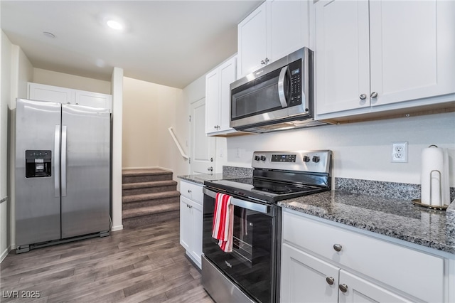 kitchen with stainless steel appliances, white cabinetry, dark stone countertops, and wood finished floors