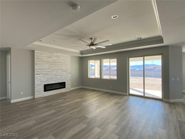 unfurnished living room with a tray ceiling, a fireplace, visible vents, and crown molding