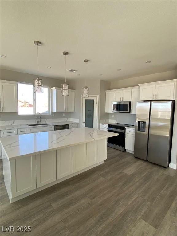 kitchen with hanging light fixtures, appliances with stainless steel finishes, white cabinets, a kitchen island, and a sink