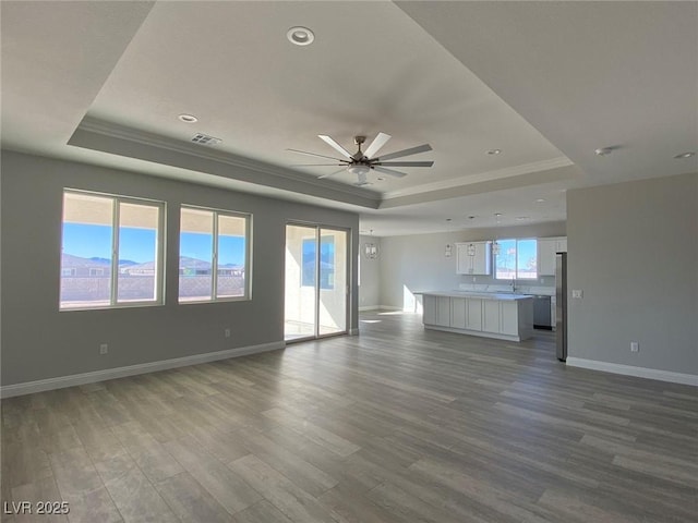 unfurnished living room with baseboards, visible vents, a raised ceiling, a ceiling fan, and light wood-style floors