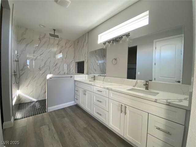 full bath with double vanity, wood finished floors, a sink, and a marble finish shower