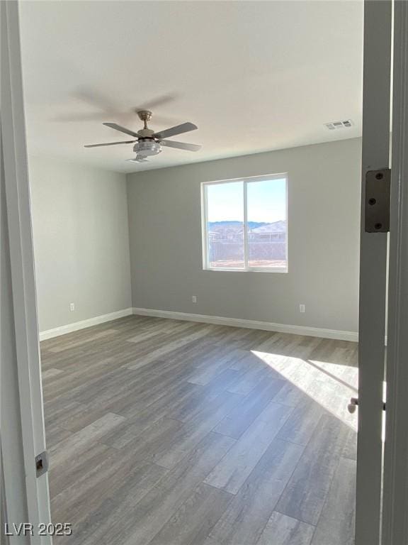 unfurnished room with ceiling fan, wood finished floors, visible vents, and baseboards