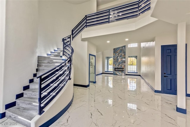 entryway featuring a towering ceiling, marble finish floor, stairs, and baseboards