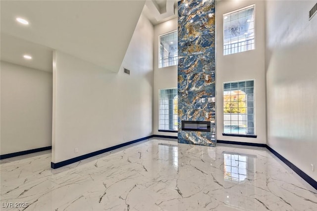 unfurnished living room with marble finish floor, plenty of natural light, and baseboards