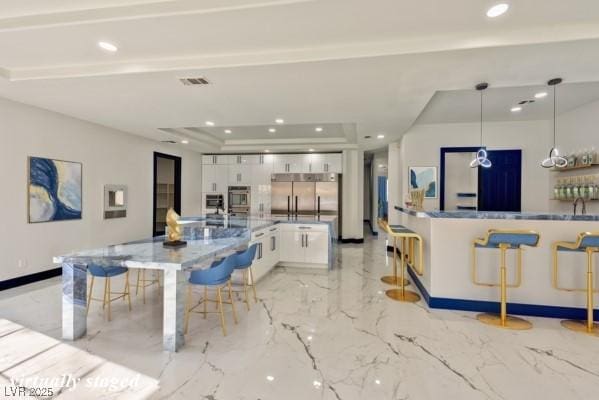 kitchen featuring white cabinetry, stainless steel built in fridge, decorative light fixtures, and a kitchen bar