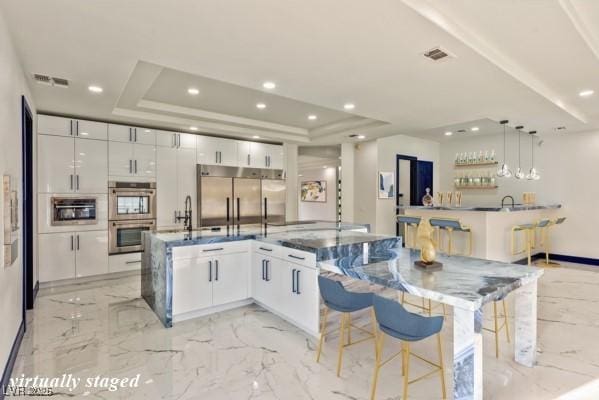 kitchen with white cabinetry, appliances with stainless steel finishes, pendant lighting, and a large island with sink