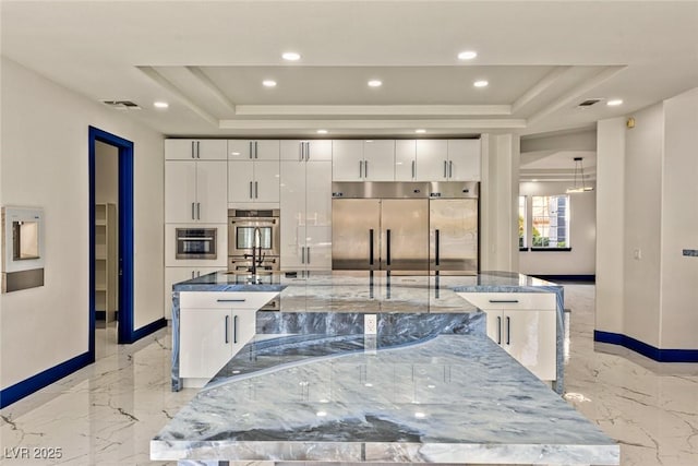 kitchen with a spacious island, a tray ceiling, and white cabinetry