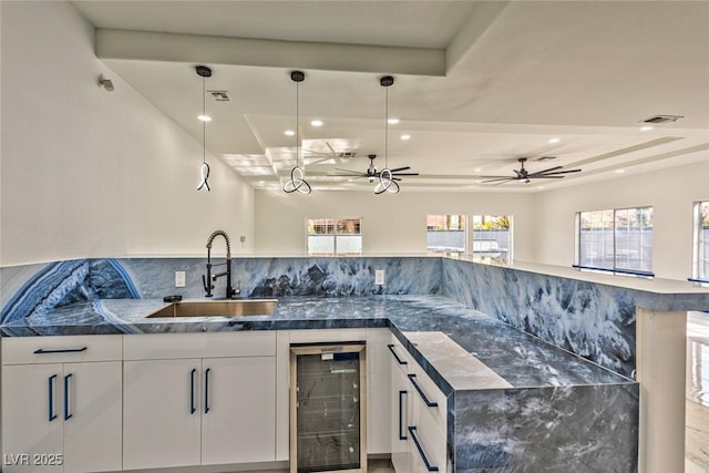 kitchen with beverage cooler, visible vents, white cabinetry, and a sink