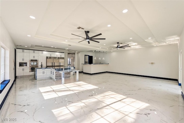 unfurnished living room with a tray ceiling, marble finish floor, visible vents, and recessed lighting