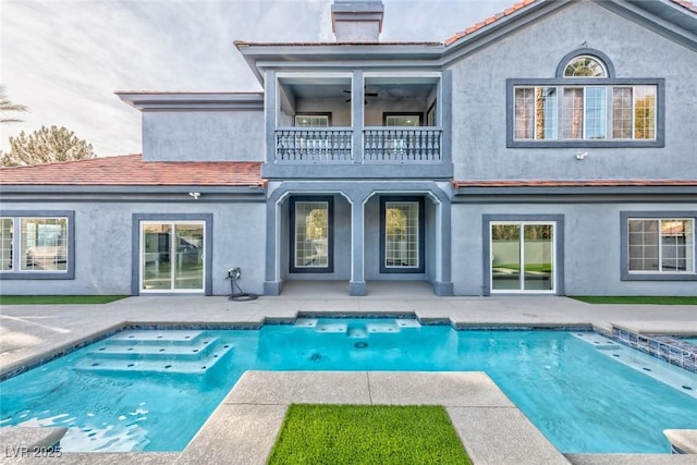 rear view of property featuring an outdoor pool, a balcony, a tile roof, a chimney, and stucco siding