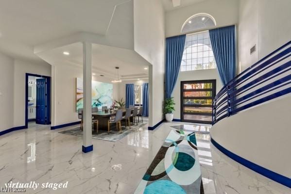 foyer featuring marble finish floor, a high ceiling, and baseboards