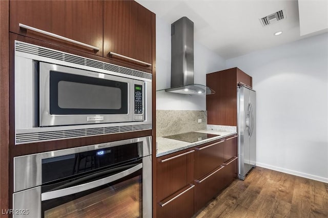 kitchen with visible vents, dark wood finished floors, wall chimney exhaust hood, appliances with stainless steel finishes, and light stone counters