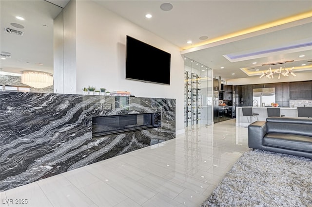 living area featuring recessed lighting, a raised ceiling, visible vents, and a high end fireplace