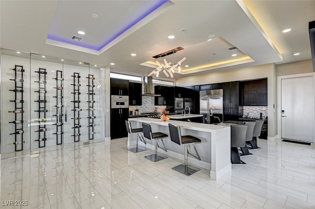 kitchen with a breakfast bar, wall chimney exhaust hood, a tray ceiling, and stainless steel appliances