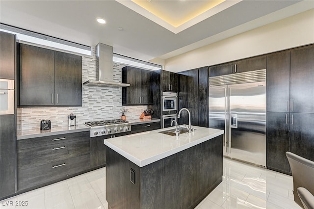 kitchen featuring tasteful backsplash, light countertops, appliances with stainless steel finishes, a sink, and wall chimney exhaust hood