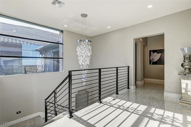 hall with baseboards, visible vents, a notable chandelier, and an upstairs landing