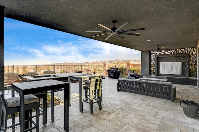 view of patio / terrace with a ceiling fan, a fenced backyard, an outdoor fireplace, outdoor dining area, and a mountain view