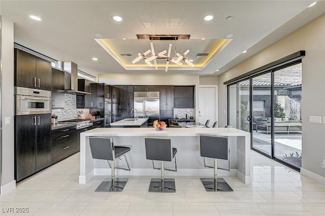 kitchen featuring wall chimney range hood, visible vents, a tray ceiling, and stainless steel appliances