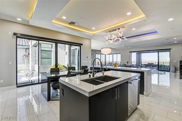 kitchen with dark cabinets, a sink, visible vents, a raised ceiling, and a center island with sink