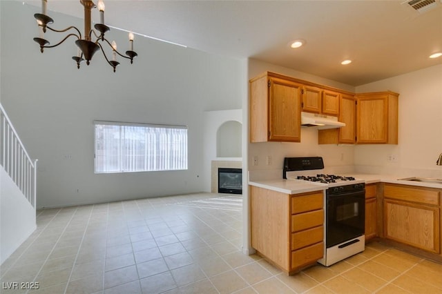 kitchen featuring light tile patterned floors, under cabinet range hood, open floor plan, light countertops, and gas stove