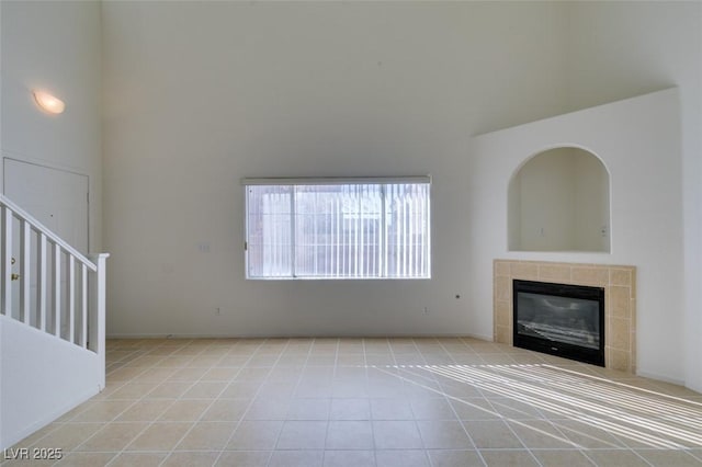 unfurnished living room with a tile fireplace, a towering ceiling, and stairs