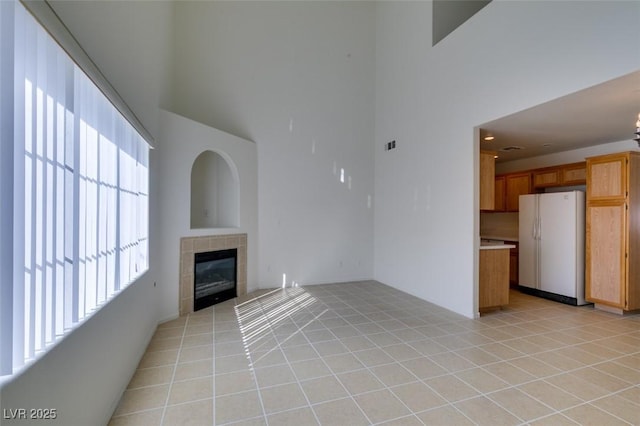 unfurnished living room with light tile patterned floors, a high ceiling, a tile fireplace, and visible vents