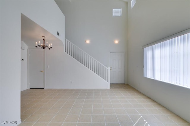 unfurnished living room with light tile patterned flooring, a notable chandelier, a towering ceiling, visible vents, and stairs