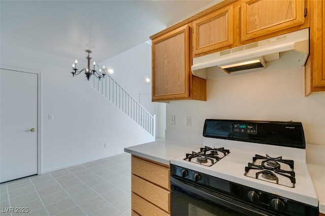 kitchen with a chandelier, light tile patterned floors, under cabinet range hood, range with gas stovetop, and light countertops