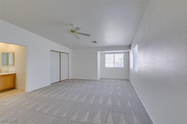 unfurnished bedroom featuring a closet, visible vents, light carpet, connected bathroom, and vaulted ceiling