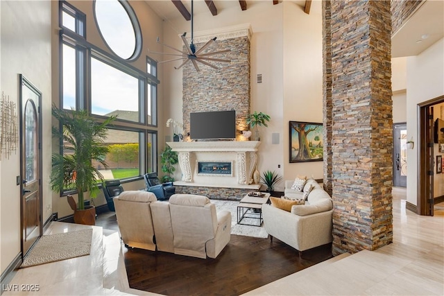 living room featuring a towering ceiling, a ceiling fan, a glass covered fireplace, wood finished floors, and beamed ceiling