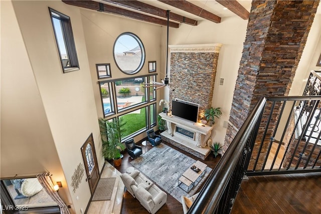 living area featuring a high ceiling, a fireplace, wood finished floors, and beam ceiling