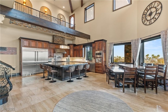 kitchen with built in appliances, under cabinet range hood, a kitchen breakfast bar, an island with sink, and dark stone countertops