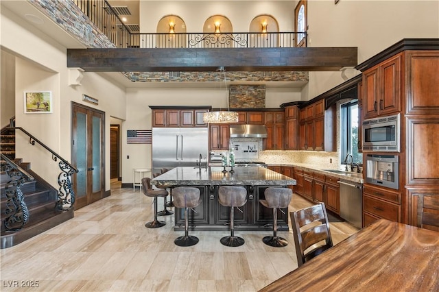 kitchen with built in appliances, a sink, a towering ceiling, a kitchen island, and dark stone countertops