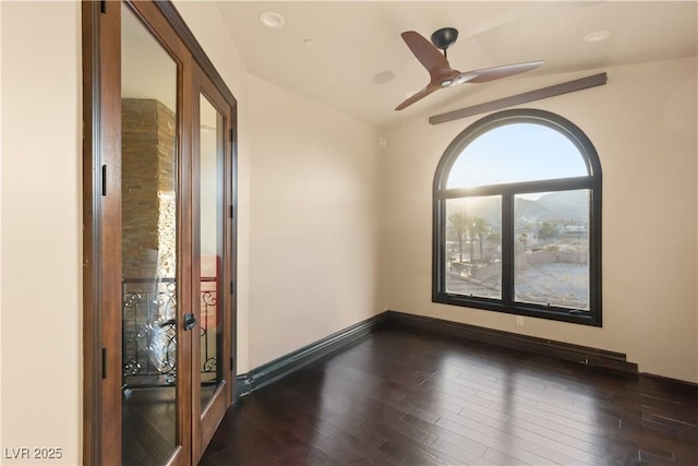 empty room featuring lofted ceiling, baseboards, dark wood finished floors, and a ceiling fan