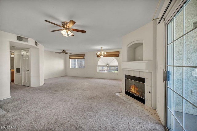 unfurnished living room featuring ceiling fan with notable chandelier, visible vents, a tiled fireplace, and light colored carpet