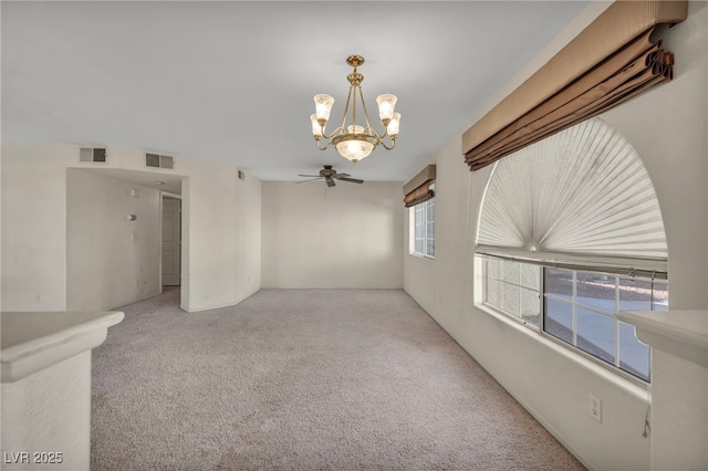 empty room featuring ceiling fan with notable chandelier, visible vents, and light colored carpet