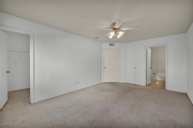 unfurnished bedroom featuring a walk in closet, a closet, visible vents, light carpet, and ensuite bath