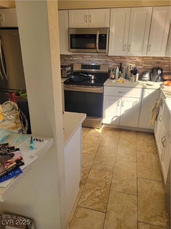 kitchen featuring stainless steel appliances, light countertops, decorative backsplash, and white cabinetry