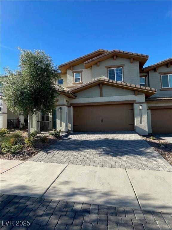 view of front facade with a garage, a tile roof, decorative driveway, and stucco siding