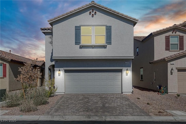 traditional home featuring decorative driveway, a tile roof, an attached garage, and stucco siding