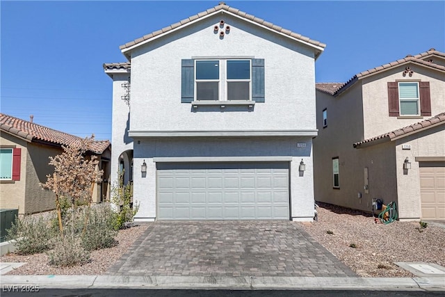 view of front facade with decorative driveway, a tile roof, an attached garage, and stucco siding