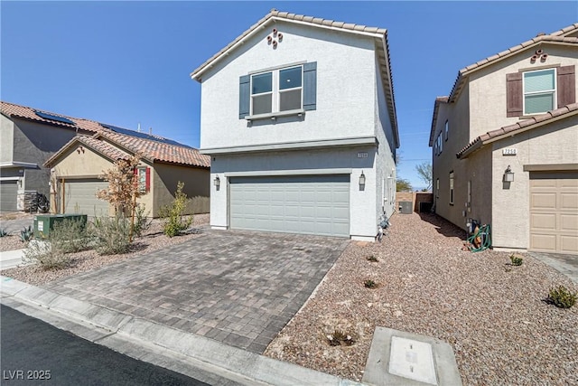 view of front facade featuring decorative driveway, a tiled roof, an attached garage, and stucco siding