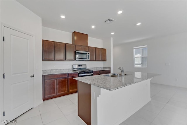 kitchen with a sink, visible vents, appliances with stainless steel finishes, light stone countertops, and an island with sink